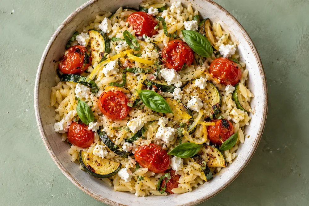 Orzo mit Zitrone, gerösteten Tomaten, Zucchini, Basilikum und Feta in einer Keramikschüssel